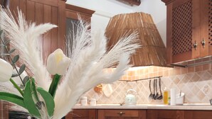 Une cuisine avec des meubles de rangement en bois, un chemin de table en tissu tissé et un vase rempli de fleurs blanches.