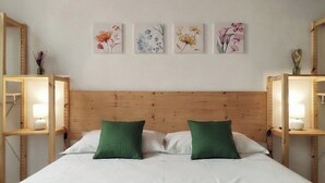 Une chambre à coucher avec une tête de lit en bois, un lit recouvert de draps blancs et agrémenté d’oreillers verts, et quatre œuvres d’art aux motifs floraux accrochées au mur.