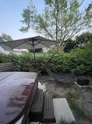 Relax in a serene outdoor space surrounded by lush greenery and a tree, with a shaded table and benches along a paved path.