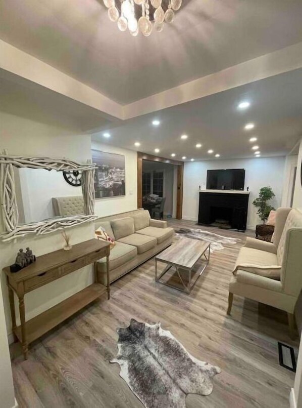 Relax in this stylish living room with a sofa set, coffee table, and armchair, featuring a large flat-screen TV and a cozy fireplace.
