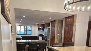 A modern kitchen with dark wood cabinets, a central island, and a dining area with a marble table and dark chairs. - 4,000 sq ft 6 bed ocean Villa w/housekeeping included!! (Mazatlán)