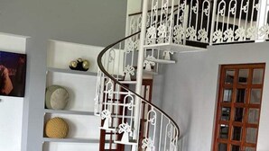 A modern living room with a black leather sofa, a small round table, and a white spiral staircase with decorative railings. - 4,000 sq ft 6 bed ocean Villa w/housekeeping included!! (Mazatlán)