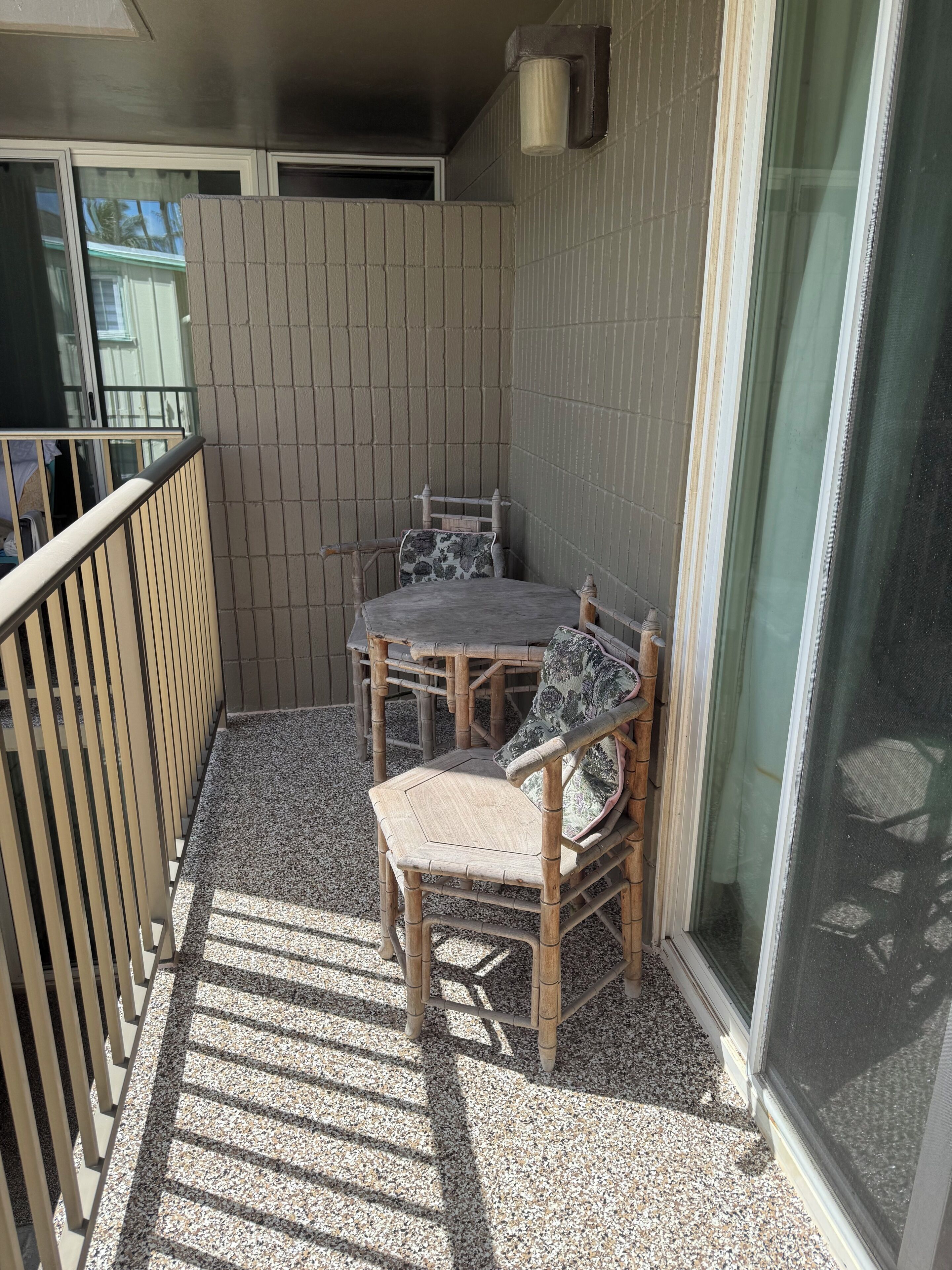Un balcon avec une table et des chaises, une balustrade et une vue à travers une porte vitrée.