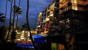 A multi-story building with balconies, surrounded by palm trees, at night. - Turtle Beachfront, snorkeling, free parking, wash-dryer in unit, New bigger AC.  (Hauula)
