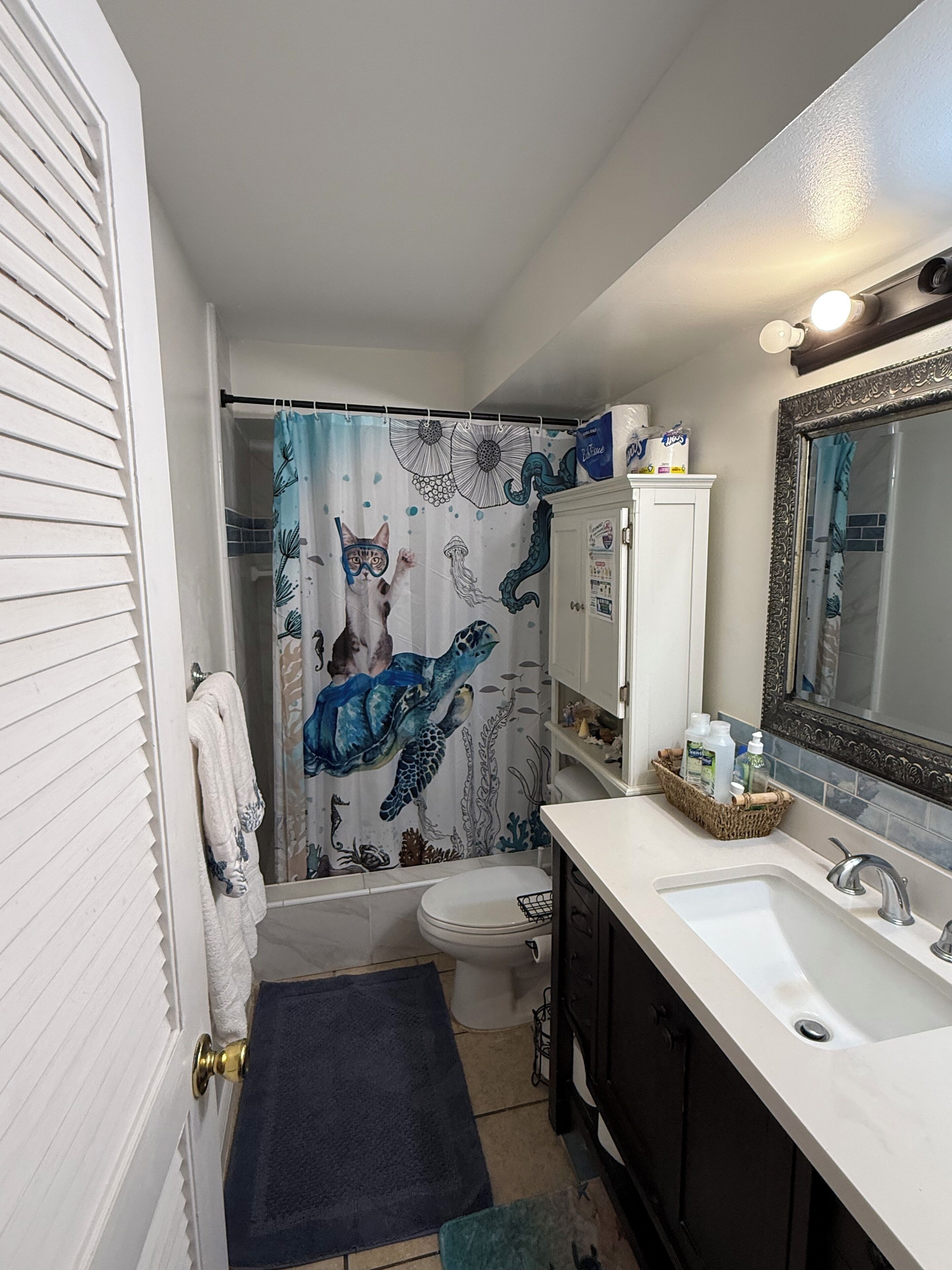 A bathroom with a shower curtain featuring a sea turtle design, a toilet, a sink with a mirror, and a towel rack.