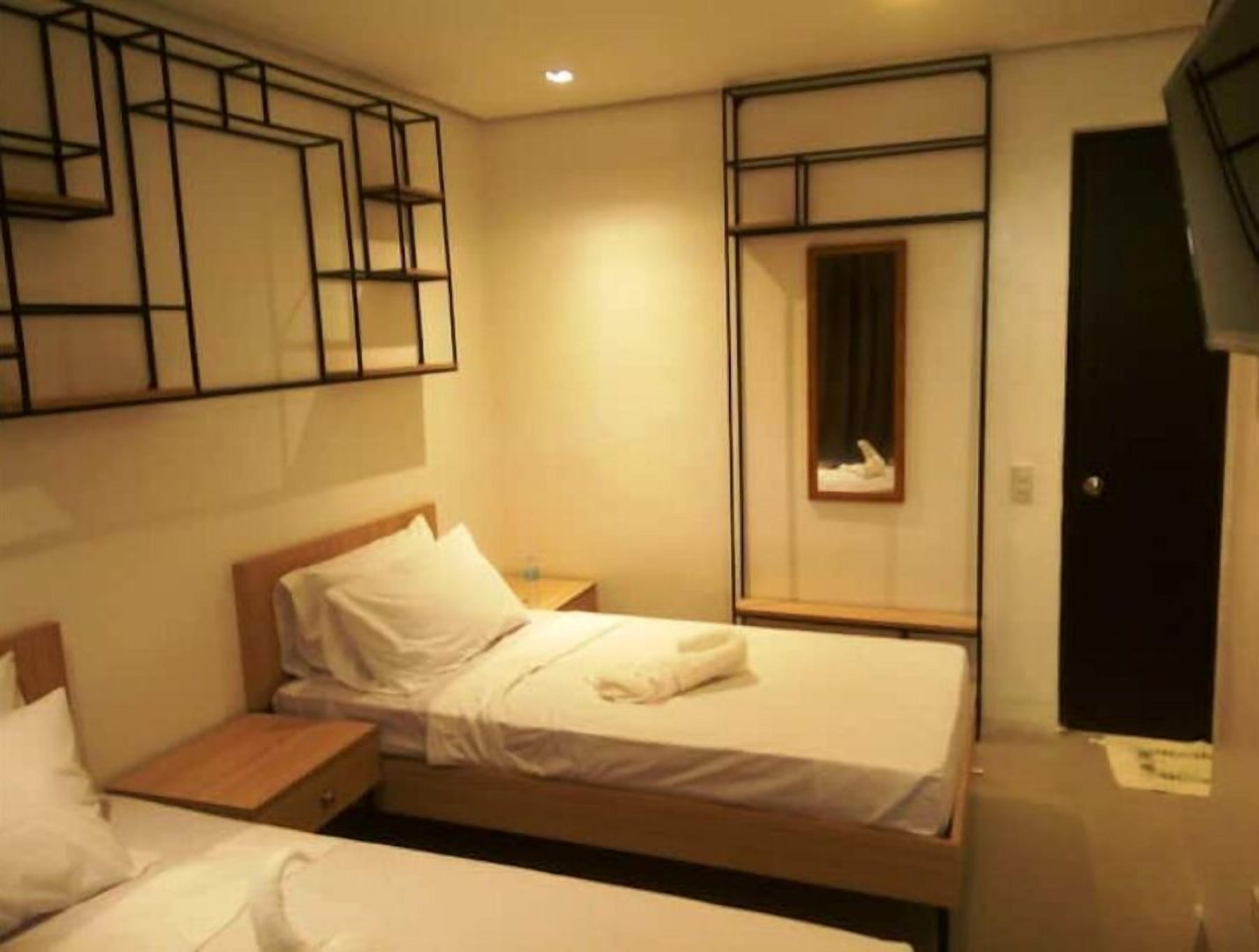 A hotel room with two beds, a wooden headboard, a bedside table, a wall-mounted shelf, and a framed picture.