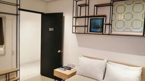Ein modernes Hotelzimmer mit einem Bett, einem Nachttisch, einer schwarzen Tür mit der Nummer 208 und einer geometrischen Wanddekoration.