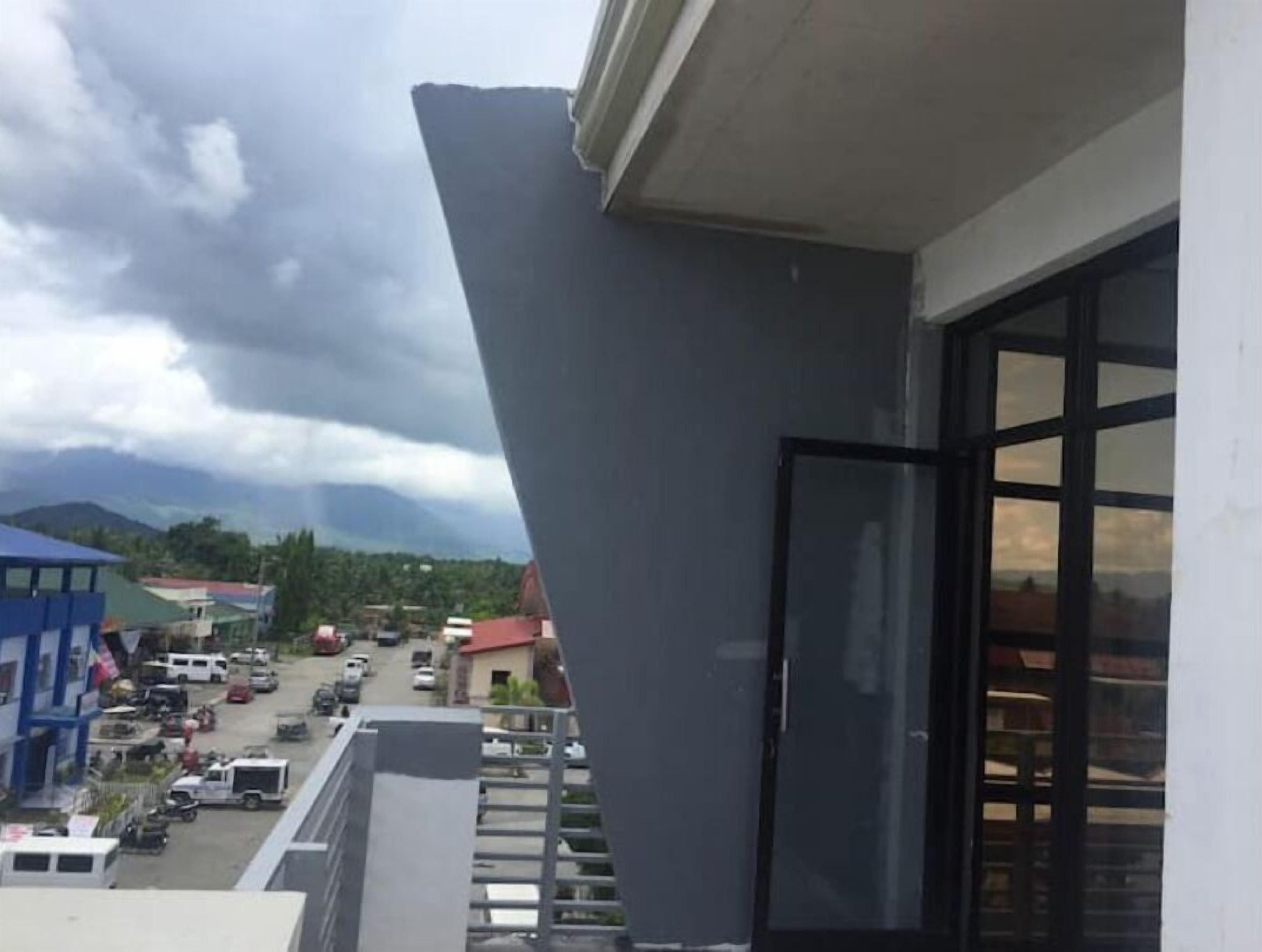 Vista de uma varanda com vista para uma rua com veículos estacionados e edifícios.