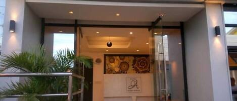 A hotel entrance with a glass door, a reception desk, and a decorative wall.