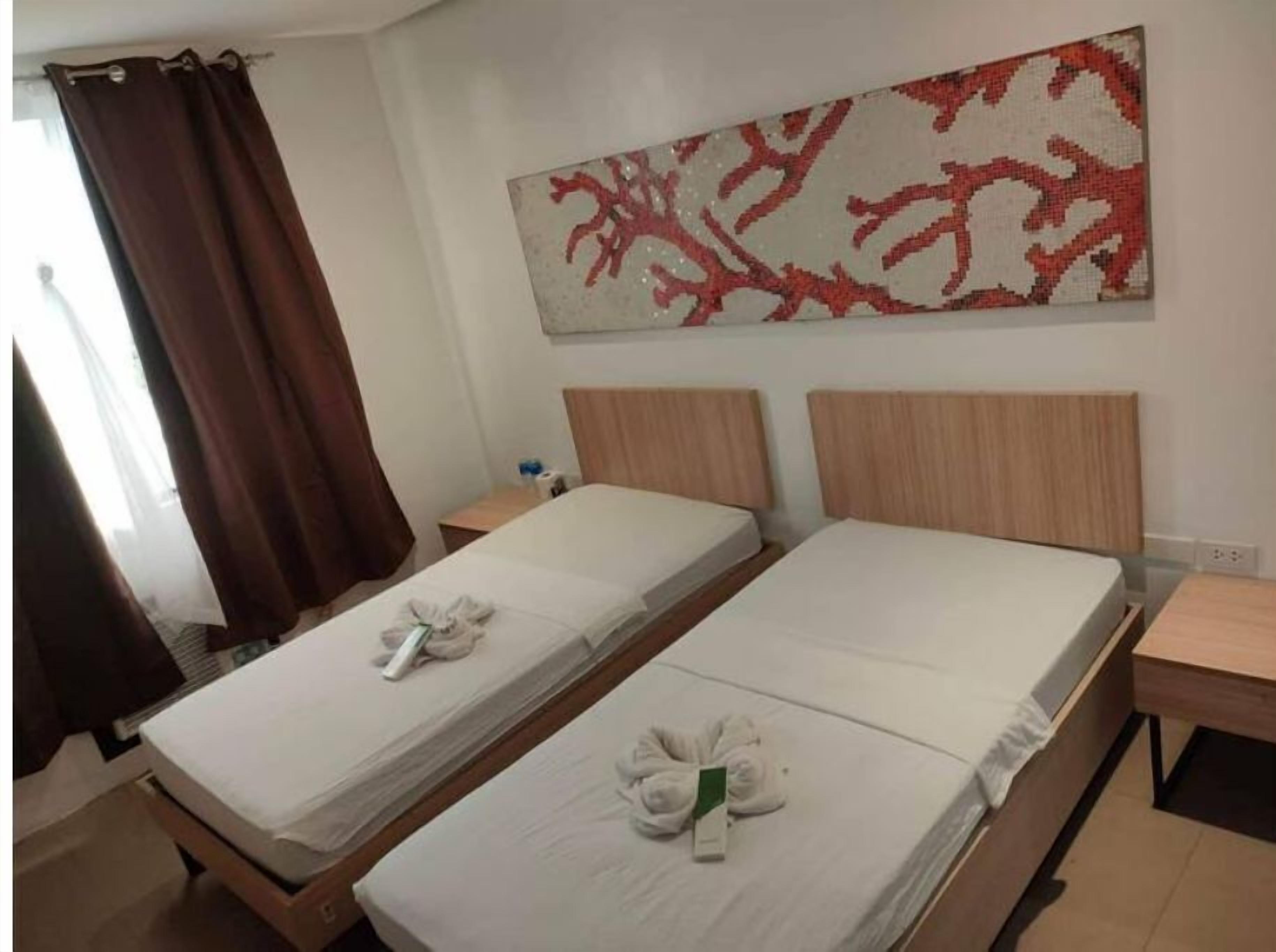 Een hotelkamer met twee enkele bedden, een houten hoofdbord, een nachtkastje met een lamp en een kunstwerk aan de muur.