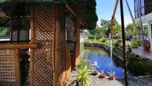 Une structure traditionnelle à toit de chaume, agrémentée d’un treillage en bois, d’un petit canal d’eau et de plantes en pot.