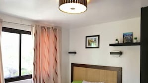 Ein Hotelzimmer mit Bett, einem fensterbelaubten Fenster, einem an der Wand befestigten Regal mit einem Bild und einem Schild auf dem Nachttisch.