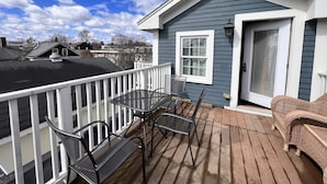 Une terrasse avec une table et des chaises, un canapé en osier et un petit bâtiment doté d’une porte et d’une fenêtre blanches.