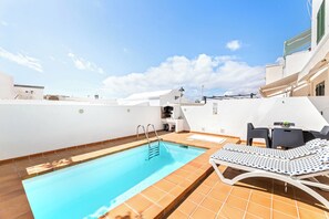 Una piscina en la azotea con aguas cristalinas, un sillón de tomar el sol y una mesa con sillas.