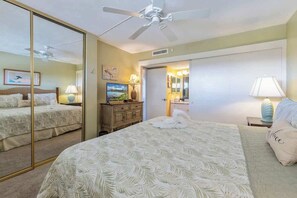 Quarto de hotel com uma cama grande, um ventilador de teto, um espelho, uma cômoda e uma televisão.