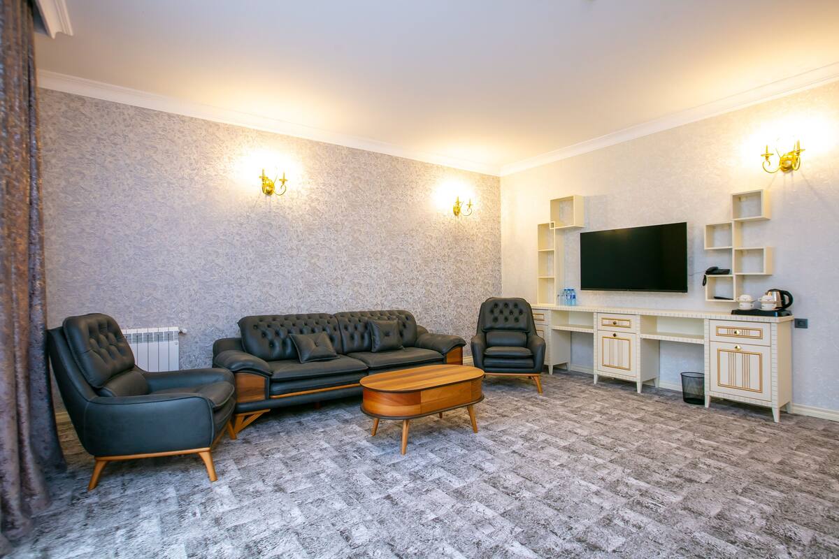 Ein Wohnzimmer mit einer Couch, zwei Sesseln, einem Couchtisch, einem Fernseher und einer kleinen Küchenzeile.