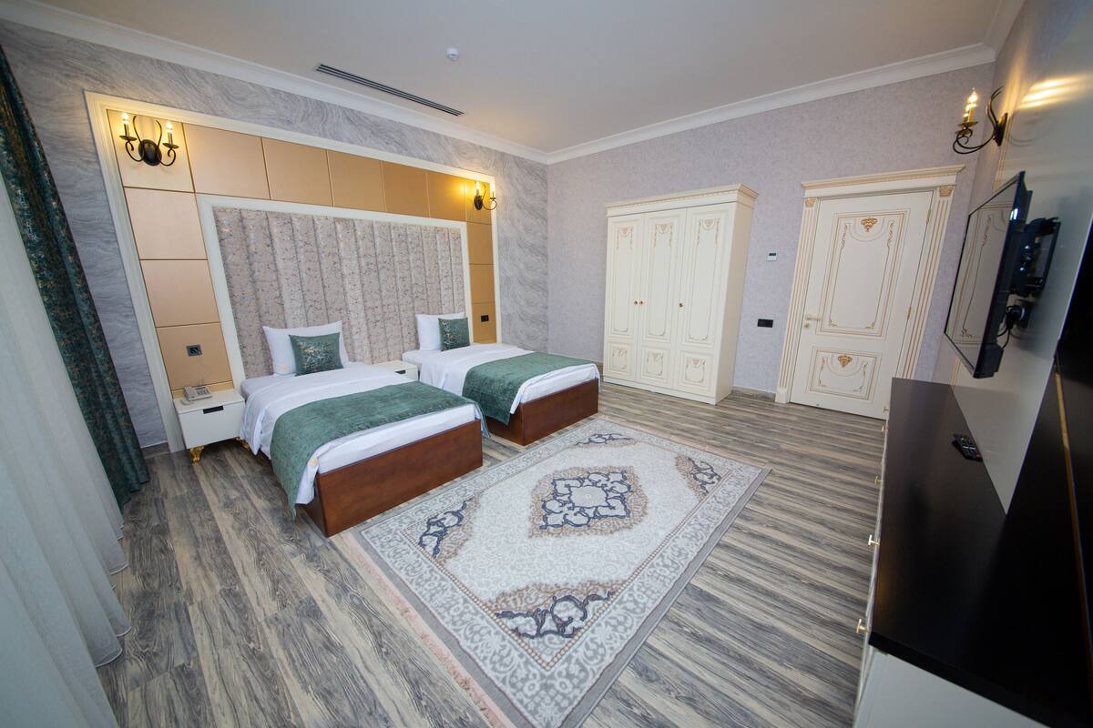 Ein Hotelzimmer mit zwei Betten, einem großen Kleiderschrank, einem Fernseher und einem gemusterten Teppich.