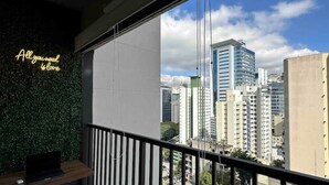 A balcony with a view of a cityscape, a neon sign on the wall, and a laptop on the counter. - Beautiful Studio near Av Paulista and Sírio Libanês (Bela Vista São Paulo)