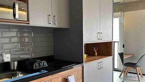 A modern kitchen with grey cabinets, a black countertop, and a built-in stove. There is a wooden shelf with a coffee maker and a small table with a chair. - Beautiful Studio near Av Paulista and Sírio Libanês (Bela Vista São Paulo)