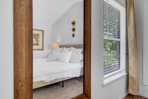 A bedroom with a bed, a lamp, a framed picture, and a window with blinds.