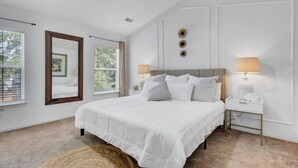 A bedroom with a large bed, two bedside tables with lamps, a ceiling fan, and a large window with blinds. - House with Backyard near the Charleston Naval Base (North Charleston)