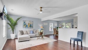 A spacious living room with hardwood flooring, a white sofa, a coffee table, and a blue chair. - House with Backyard near the Charleston Naval Base (North Charleston)