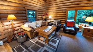 Ein gemütliches Blockhaus-Interieur mit einer Couch, Sesseln, einem Couchtisch und einem Kamin.