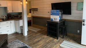 Une cuisine compacte avec des meubles blancs, un four encastré et un four à micro-ondes. Il y a un petit coin repas avec une table et des chaises.