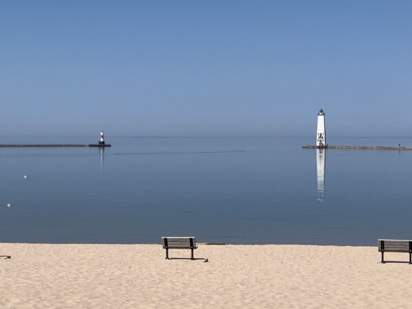 A beach with two benches and a lighthouse in the distance.