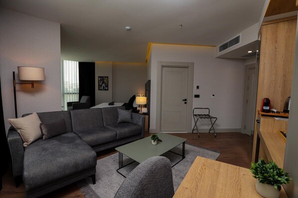 A modern living room with a grey sofa, a small coffee table, and a lamp. There is a door and a small table with a plant.