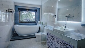 Een moderne badkamer met een vrijstaand bad, een grote spiegel en een raam met uitzicht op groen.