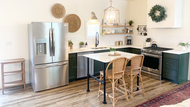Una cocina moderna con un refrigerador de acero inoxidable, una estufa empotrada y un comedor con sillas de mimbre.