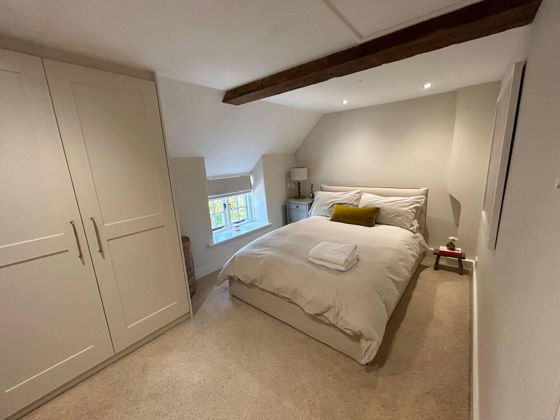 Un dormitorio con una cama grande, un armario, una ventana y una mesita de noche.