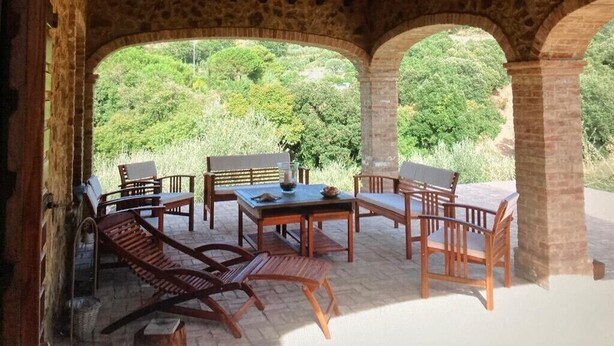 Un espacio de estar al aire libre cubierto con paredes y arcos de piedra, con vistas a un paisaje verde exuberante.