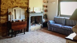 Una sala de estar acogedora con una pared de piedra, una chimenea, un sofá a rayas y una mesa de madera con una lámpara.
