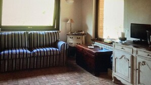 Una sala de estar acogedora con un sofá a rayas, un armario de madera, un televisor y una ventana con vistas.