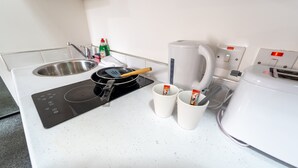 Una cocina con un lavamanos, una estufa, un hervidor y dos tazas.