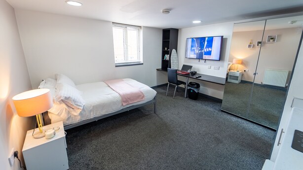 Una habitación de hotel moderna con una cama individual, un escritorio con una computadora portátil, un televisor y un armario.