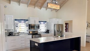 Une cuisine moderne avec des meubles blancs, un îlot central, des appareils en acier inoxydable et un plafond en bois.