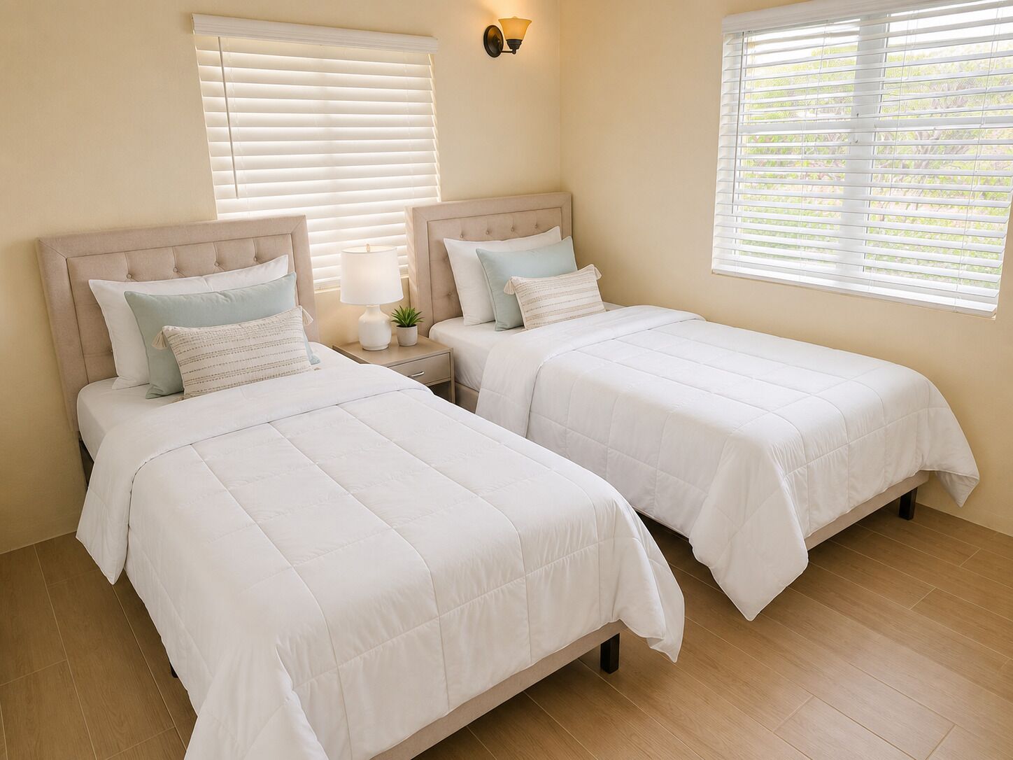 A bedroom with two beds, a nightstand with a lamp, and a wall-mounted light fixture.
