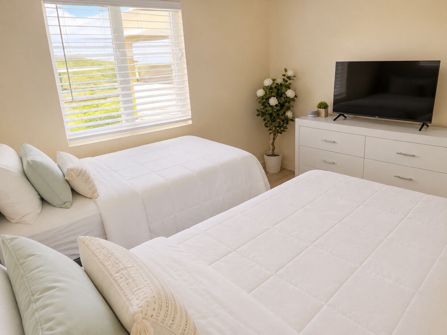 Un dormitorio con dos camas, televisión, cómoda y ventana con persianas.