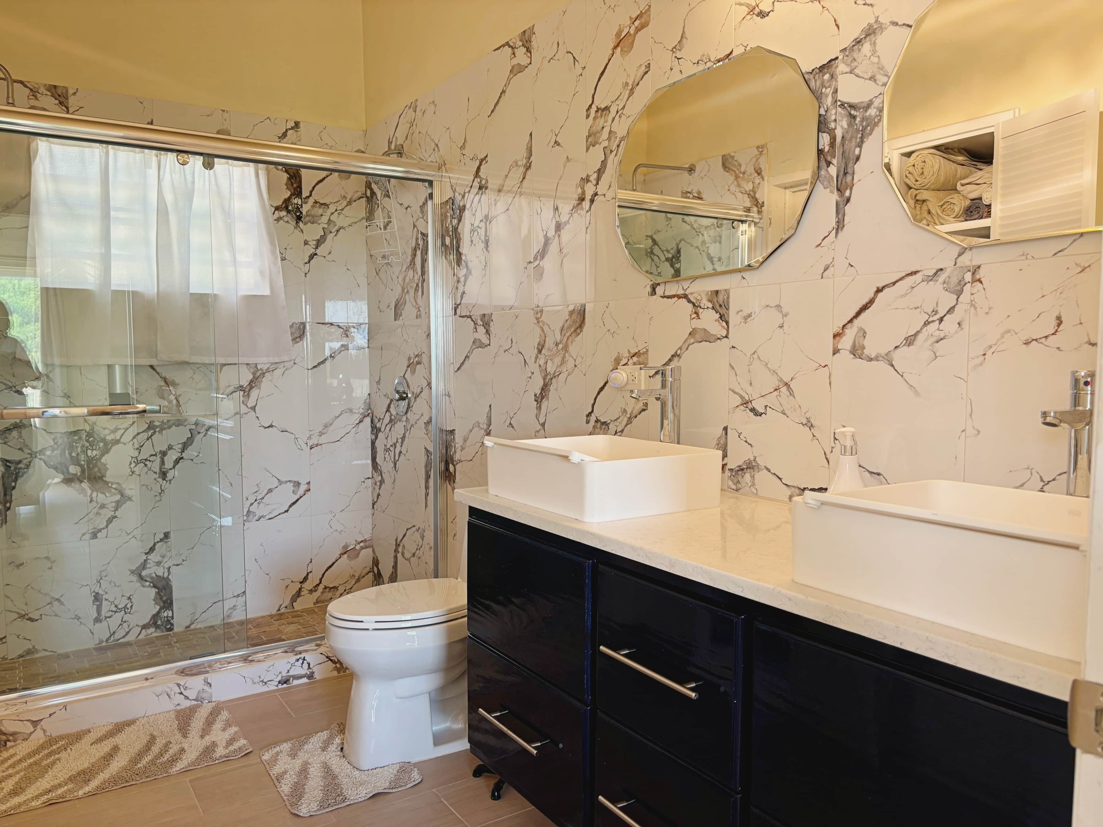 Une salle de bain dotée d’une douche à parois de verre, de toilettes, d’un lavabo avec un pare-éclaboussures en marbre et d’un meuble-lavabo avec des tiroirs.