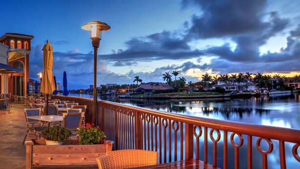 An outdoor patio with tables and chairs, a view of a body of water, and a building with a balcony. - Villa Bellevue - Beautiful lakefront rental with pool with 3 bedroom & 2 bath (Naples)