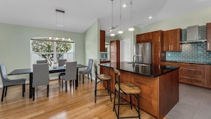 A modern kitchen with wooden cabinets, a stainless steel refrigerator, and a dining area with a table and chairs. - Villa Bellevue - Beautiful lakefront rental with pool with 3 bedroom & 2 bath (Naples)