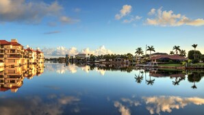 A waterfront hotel with multiple buildings reflecting in calm water, surrounded by palm trees and a clear sky. - Villa Bellevue - Beautiful lakefront rental with pool with 3 bedroom & 2 bath (Naples)