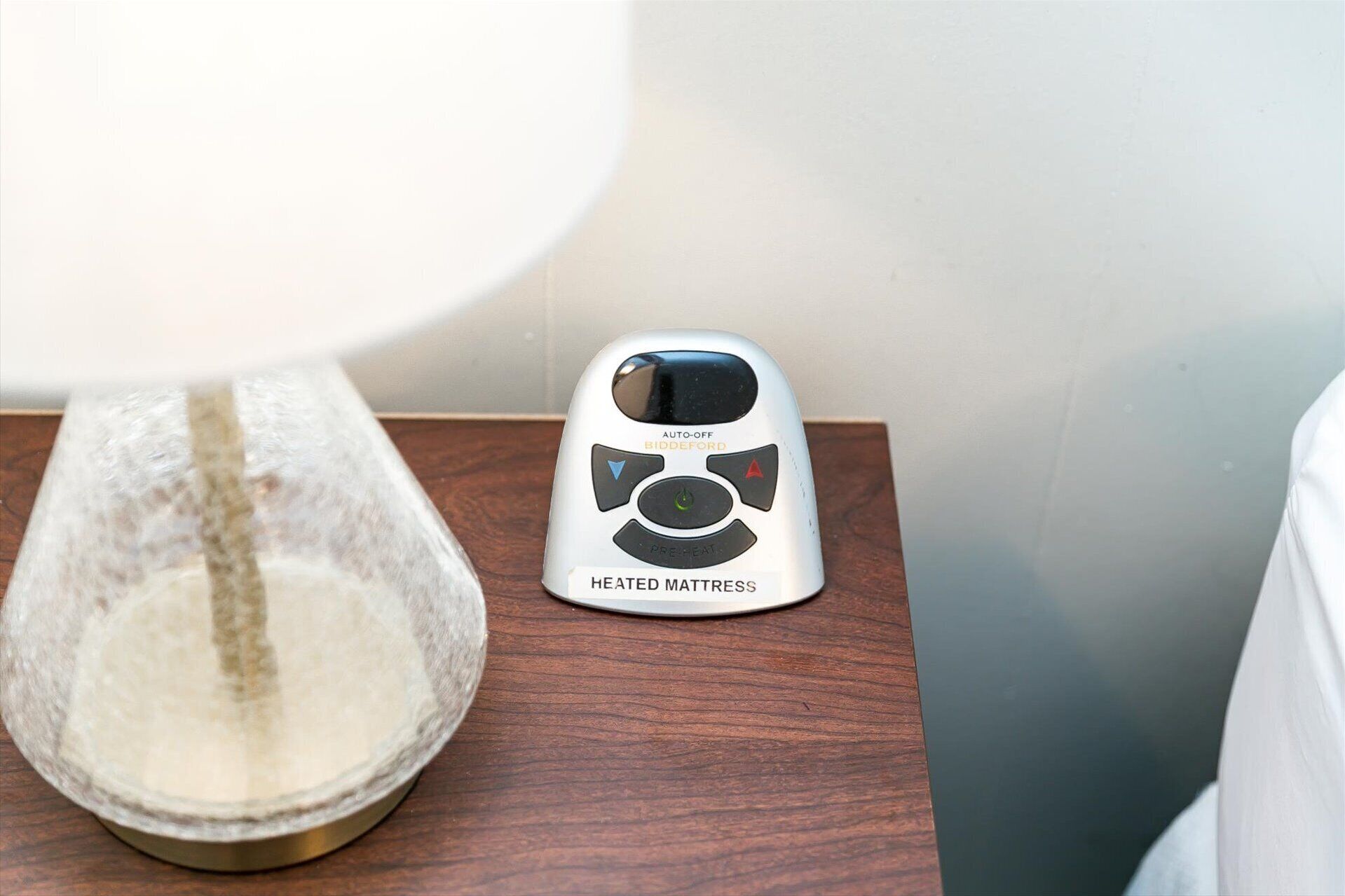 A heated mattress on a wooden nightstand next to a lamp.