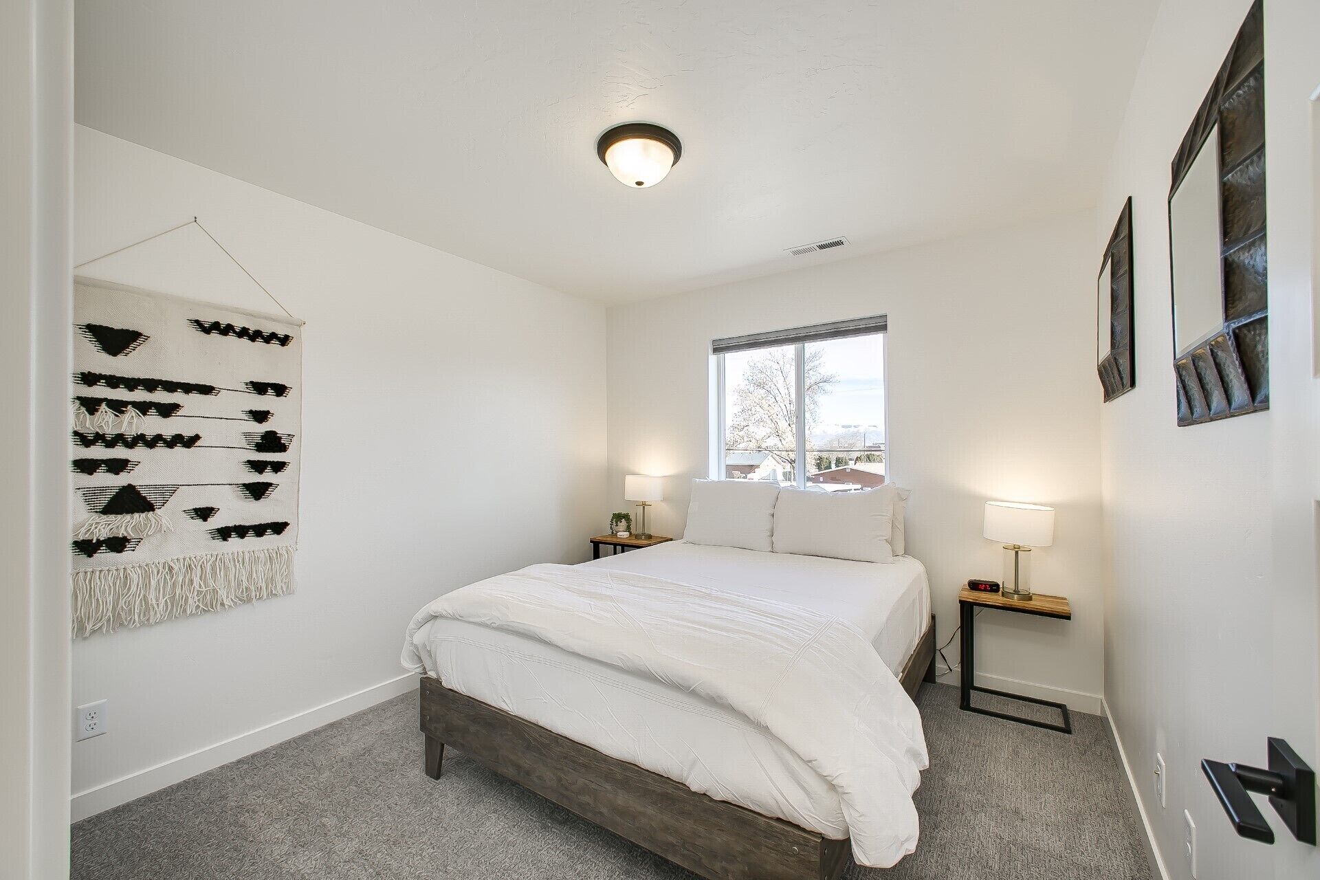 A bedroom with a bed, a window, a wall-mounted lamp, and a decorative wall hanging.