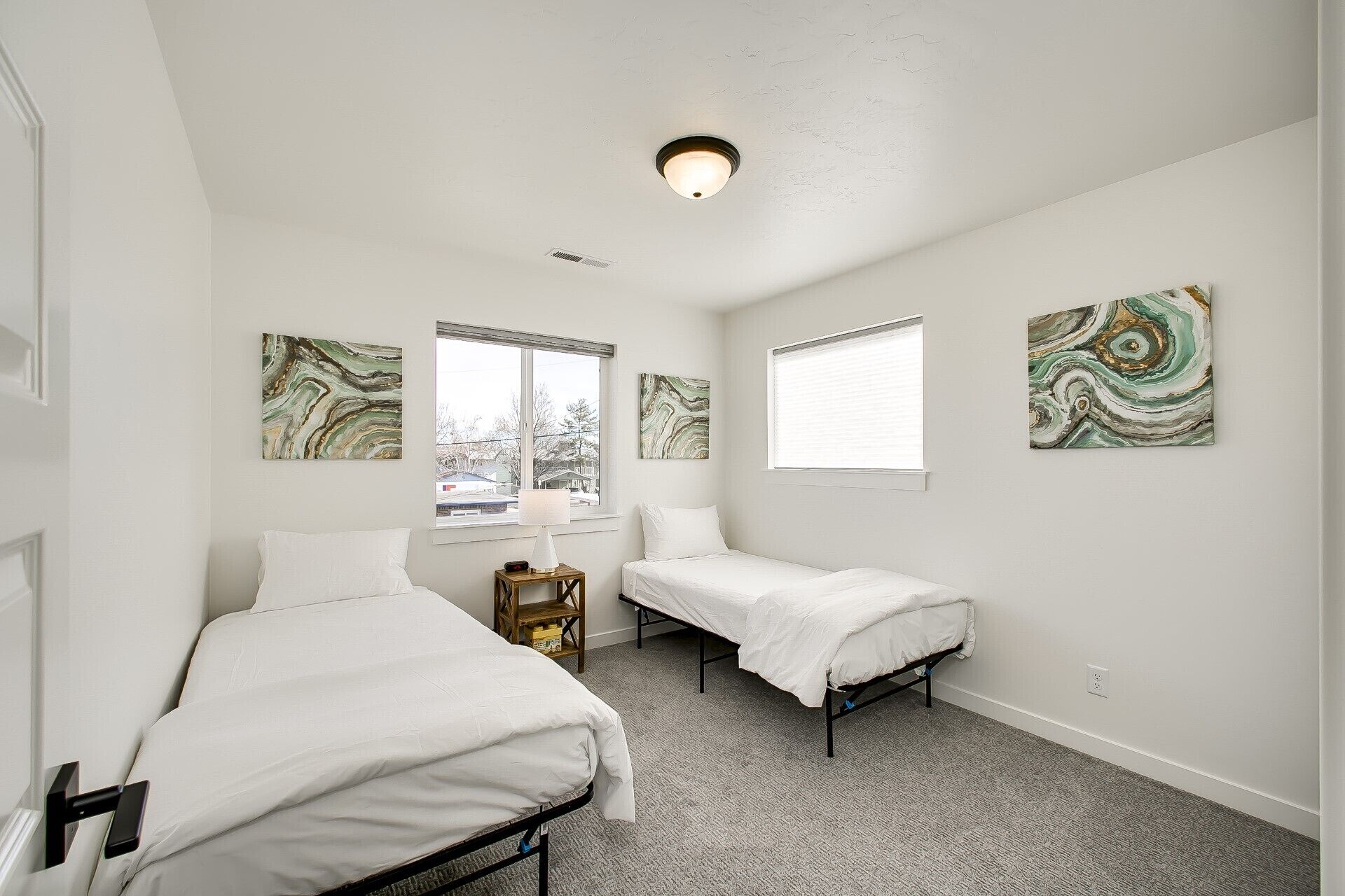 A bedroom with two beds, a window, and abstract art on the walls.