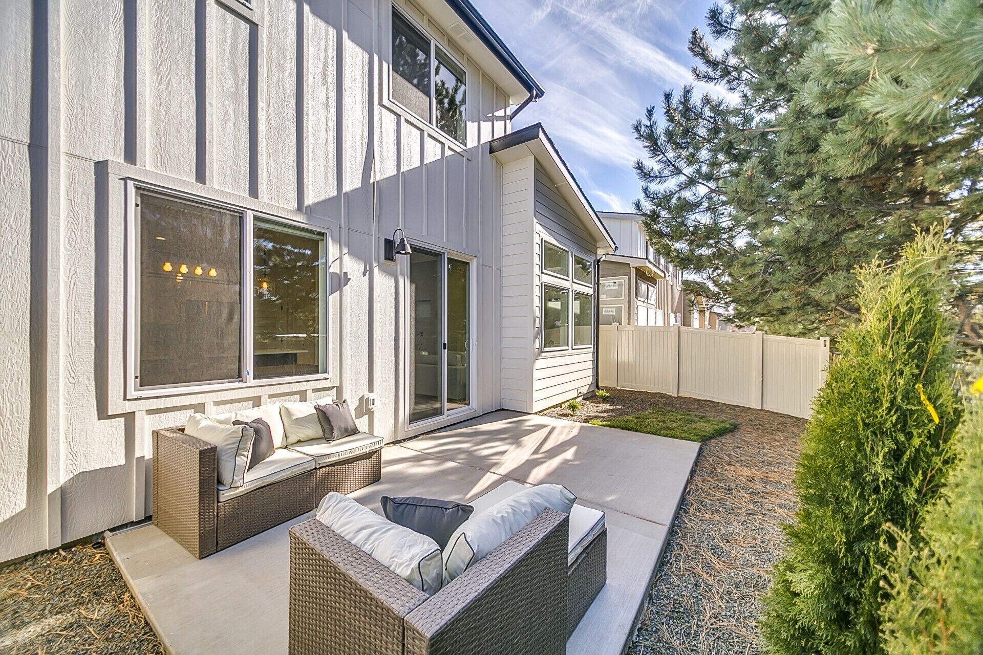 Une maison moderne dotée d’un patio aménagé avec du mobilier d’extérieur et offrant une vue sur le jardin arrière.