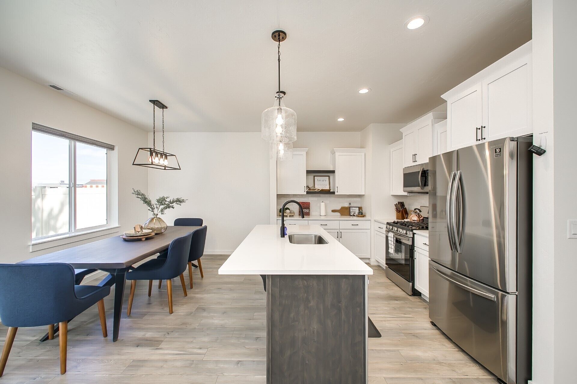 A modern kitchen with a central island, stainless steel appliances, and a dining area with blue chairs.